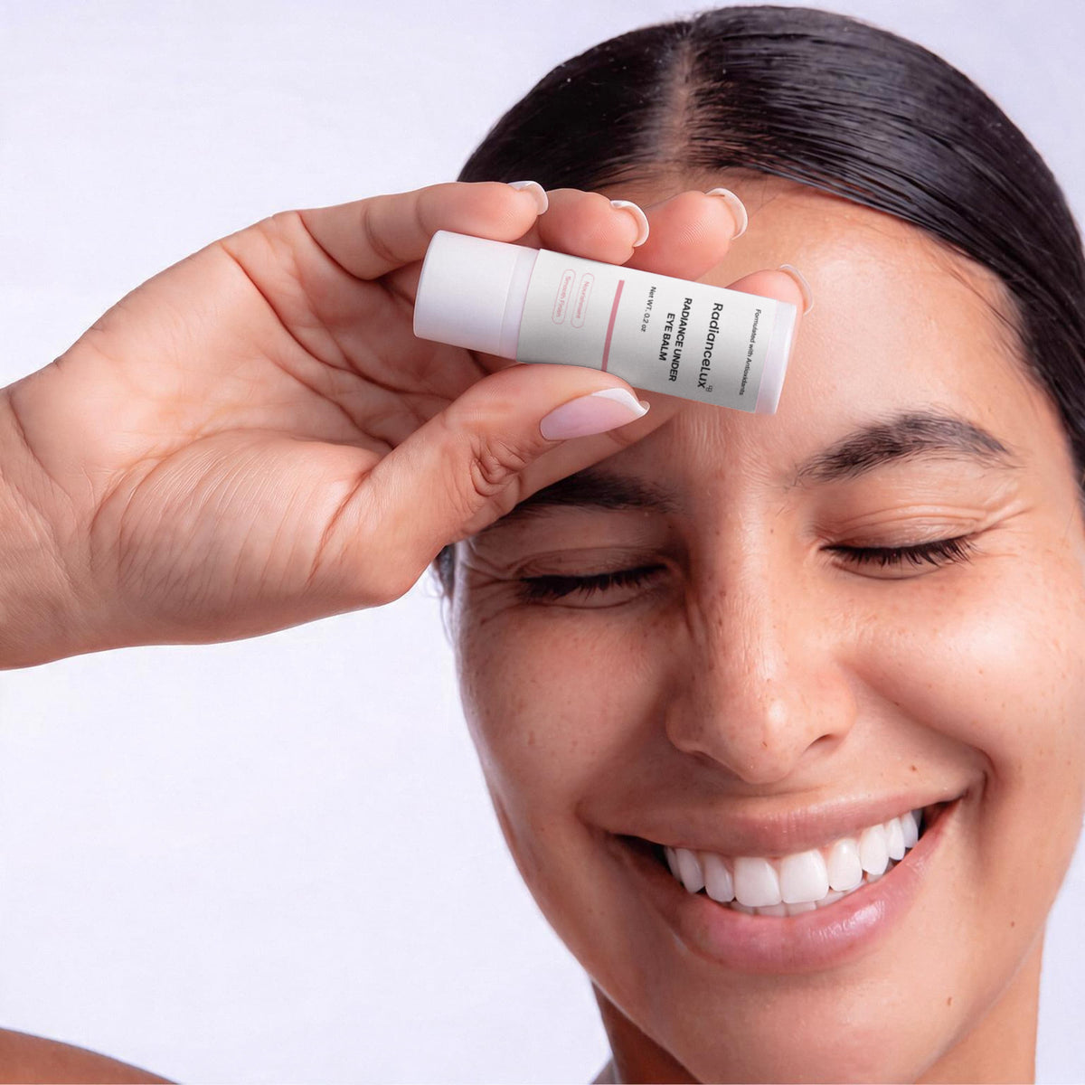Smiling woman holding the Radiance Under Eye Balm stick against her forehead