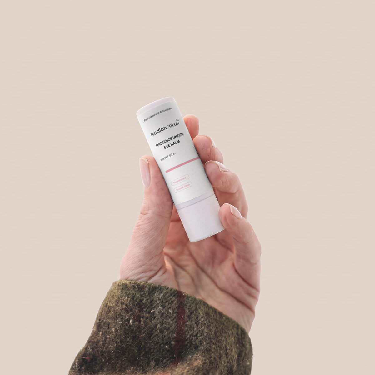 Hand holding the Radiance Under Eye Balm stick against a warm beige background