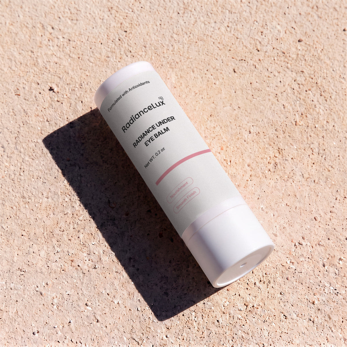 Radiance Under Eye Balm stick lying on sandy ground in bright sunlight