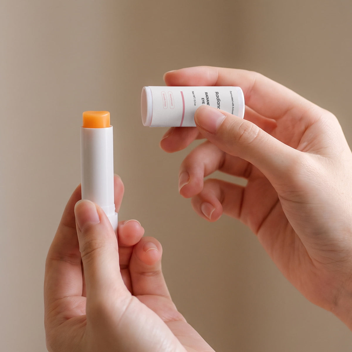 Hands twisting up the Radiance Under Eye Balm stick to show the orange balm and cap