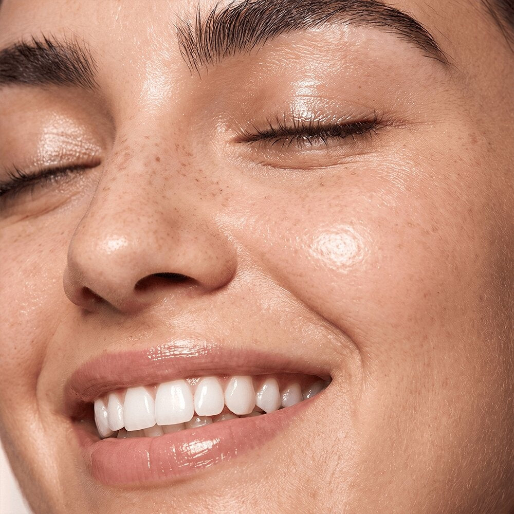 Close-up of a smiling woman with closed eyes and a soft, dewy-looking complexion