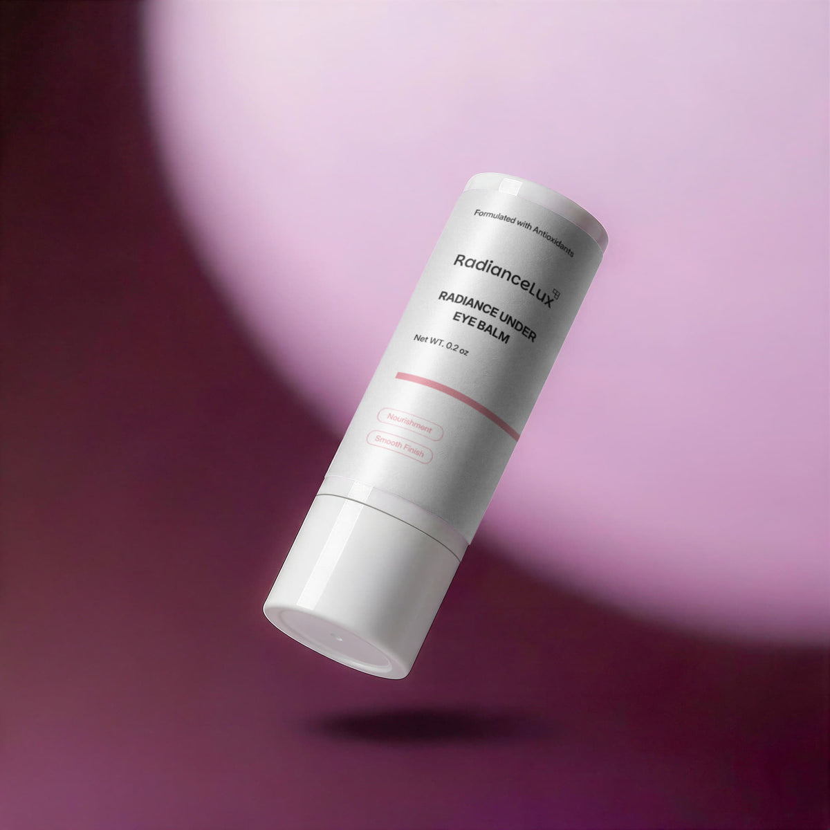 Radiance Under Eye Balm stick floating at an angle in front of a plum and pink backdrop