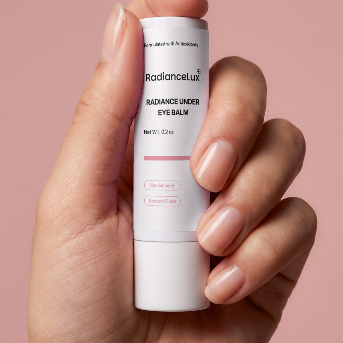 Hand holding the Radiance Under Eye Balm stick against a dusty pink background